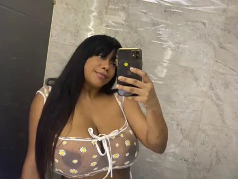 Tyfaniebony — Smiling woman in a white daisy print sheer crop top taking a selfie in a modern marble bathroom.