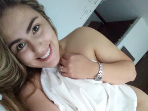 PamelaFI0RI smiles while wrapped in a white sheet, showing her bare shoulders and chest with her blonde hair down.