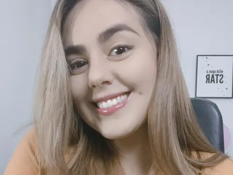 PamelaFI0RI — PamelaFI0RI smiles close-up, showing her teeth and long blonde hair while wearing an orange top.