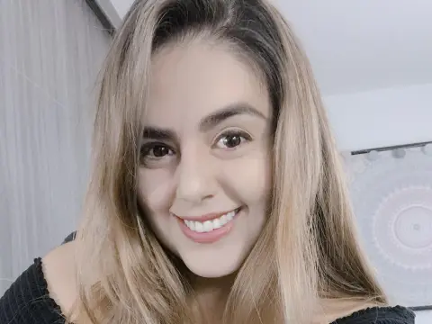 PamelaFI0RI — PamelaFI0RI smiling with long blonde hair, wearing a black off-the-shoulder top in a bright room.