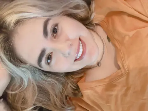 PamelaFI0RI — PamelaFI0RI smiles while lying down, showing her blonde hair and wearing an orange t-shirt.
