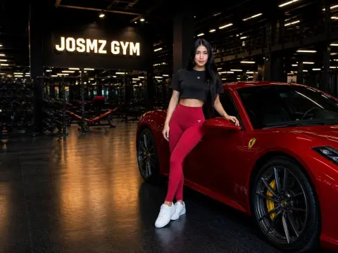 Athletic woman in red leggings and black crop top leaning on a red luxury sports car inside a modern gym.