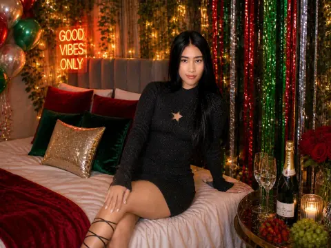 Young woman in a black long-sleeve dress sitting on a bed with festive red and green decorations.