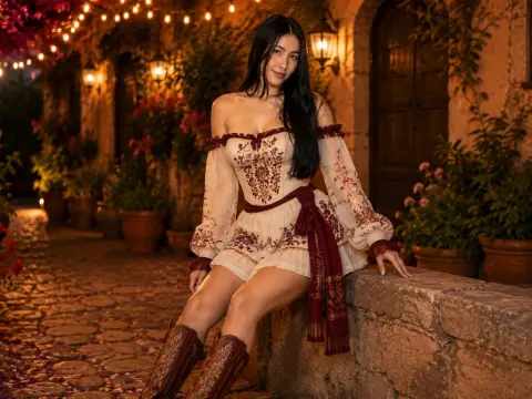 Young woman in a white off-the-shoulder floral dress sitting on a stone ledge in a warm, romantic garden setting.