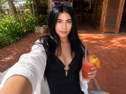 Young woman in a black bodysuit and white cardigan enjoying a refreshing fruit cocktail on a sunny patio.
