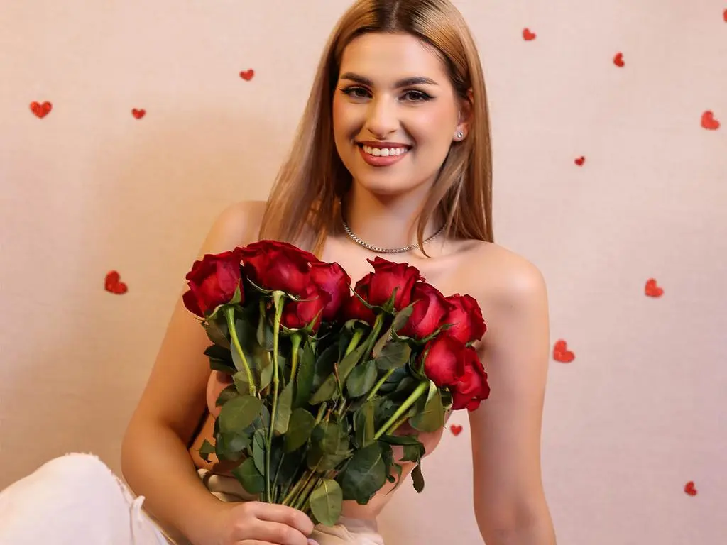 Smiling young woman in white outfit holding a large bouquet of red roses against a romantic heart background.