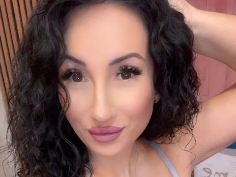 Close-up portrait of a woman with curly dark hair and natural makeup posing in a bright indoor setting.
