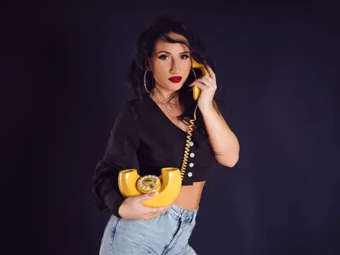 Stylish woman in a black crop top holding a vintage yellow rotary phone against a dark studio background.