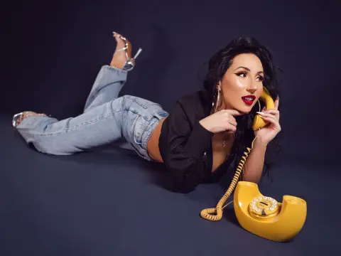 Stylish woman in denim jeans and black top lying on dark background holding a vintage yellow telephone.
