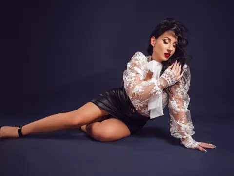 Elegant woman in a white lace blouse and black leather skirt posing against a dark studio background.