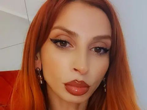MinnieDrew — Redheaded woman with glamorous winged eyeliner and glossy lips posing for a close-up portrait.
