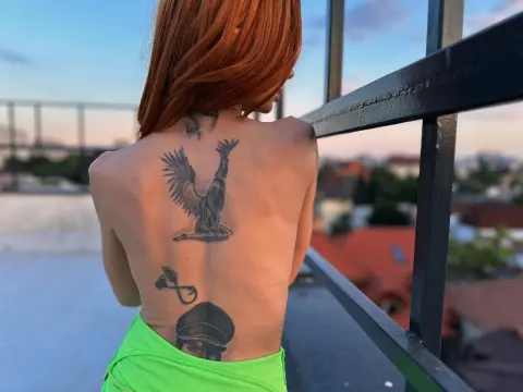 MinnieDrew — Redheaded woman with back tattoos wearing lime green clothing on a rooftop balcony at sunset.
