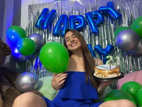 Smiling woman in a blue dress celebrating her 21st birthday with green and silver balloons and cake.