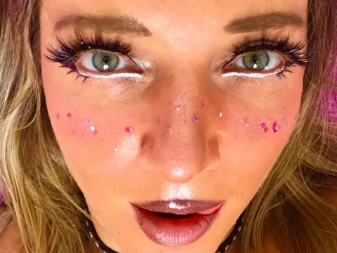 Huanshulann looks into the camera with long eyelashes, glittery pink sparkles on her cheeks, and dark lipstick.