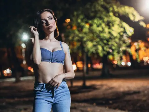 Young woman in a blue denim crop top and jeans posing outdoors at night under soft street lighting.