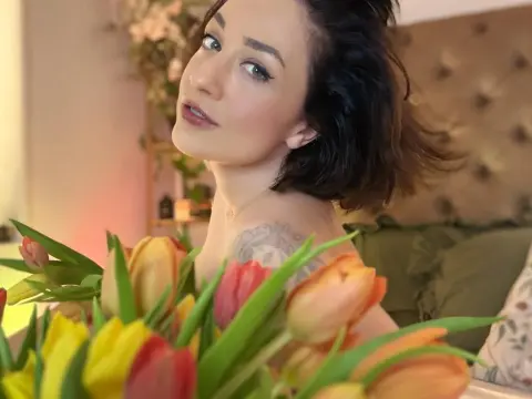 Smiling woman with dark hair posing with colorful tulips in a cozy, sunlit bedroom setting.