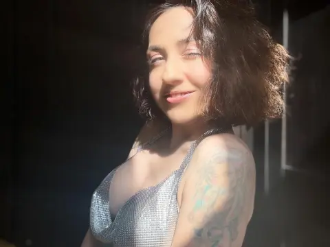 Smiling woman in a silver sequin top enjoying warm sunlight in a moody, dark indoor setting.