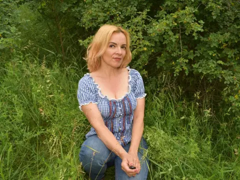 KateConner wearing a blue and white checkered puff-sleeve top and jeans while sitting in tall green grass outdoors.