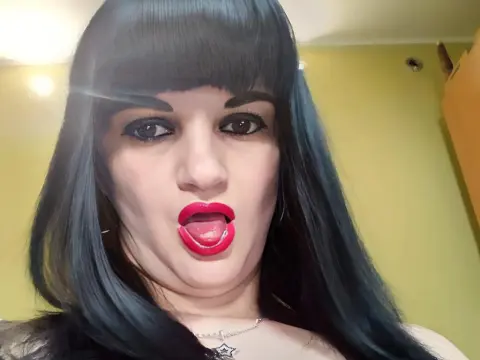 Woman with long black hair and red lipstick making a playful expression in a bright indoor setting.
