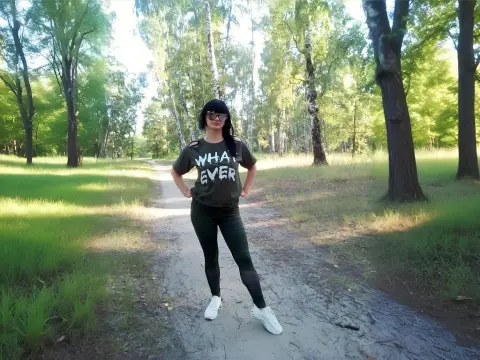 Young woman in a graphic t-shirt and leggings standing on a sunny forest path wearing sunglasses.