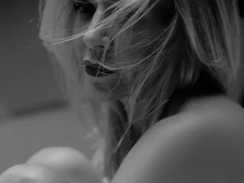 Alessandra933 — Close-up black and white portrait of a blonde woman with wind-swept hair in a moody, cinematic setting.