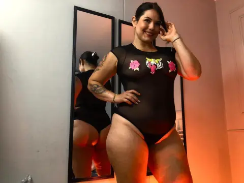 SimoneCallen — Smiling woman in a black sheer bodysuit with rose graphics posing in front of a mirror.