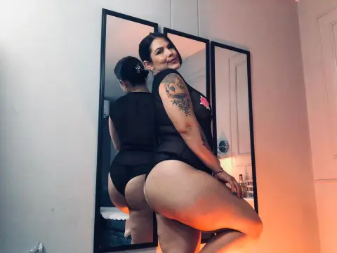 SimoneCallen — Curvy woman with tattoos in a black bodysuit posing confidently in a mirror reflection.