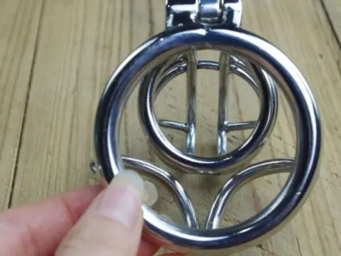 NikkiMistress — Hand holding a silver metal ring massage tool on a rustic wooden surface.