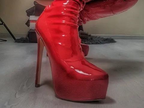 Close-up of shiny red patent leather platform high heel boots in a modern indoor setting.