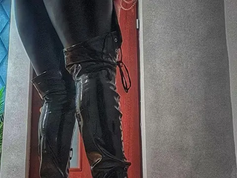 Close-up of a person wearing shiny black patent leather thigh-high boots in a modern indoor setting.