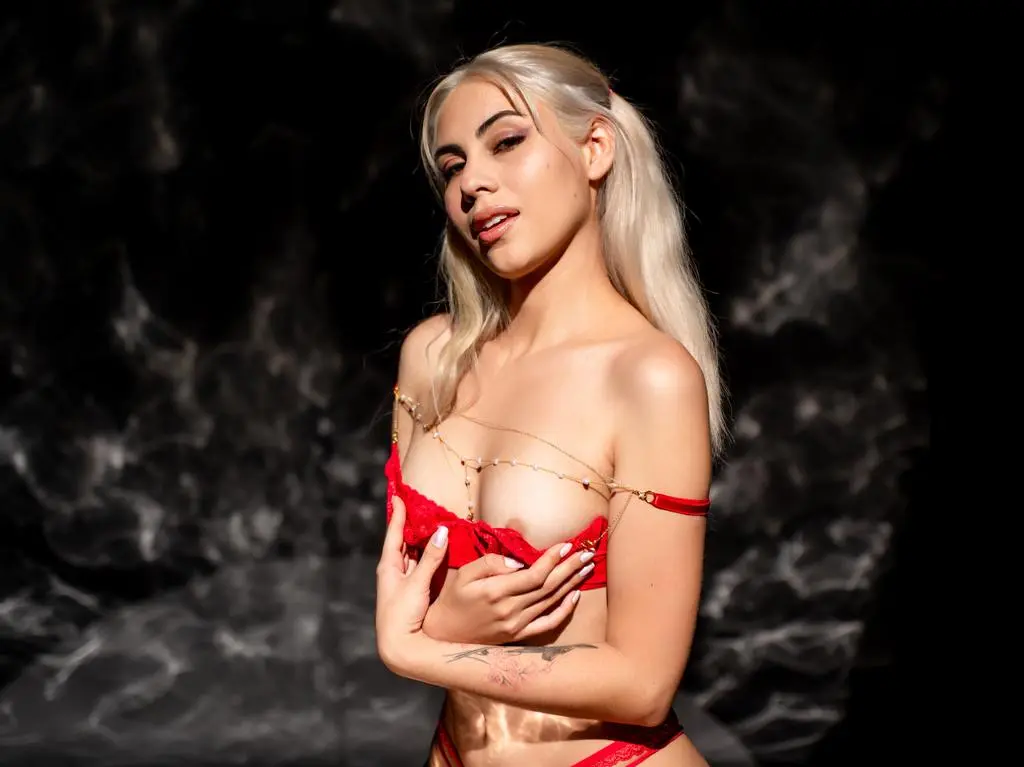 Blonde woman in red lace lingerie posing against a dark smoky background with moody lighting.