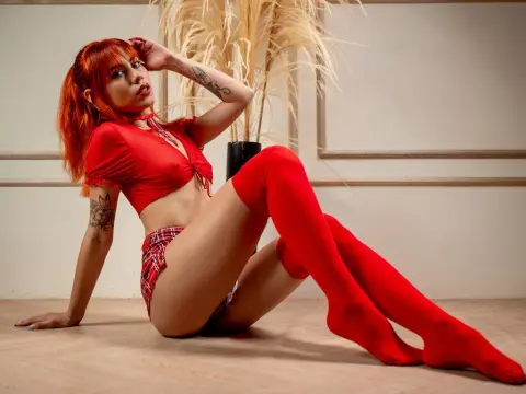 Redheaded woman in a red crop top and shorts sitting on a floor in a minimalist indoor setting.