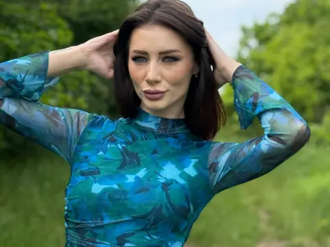 AngieShae — Woman in a blue patterned long-sleeve blouse posing in a lush green outdoor garden setting.