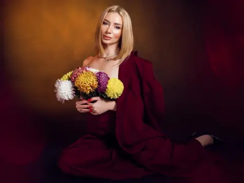 AngieShae — Elegant blonde woman in a burgundy outfit holding a colorful flower bouquet against a warm studio background.