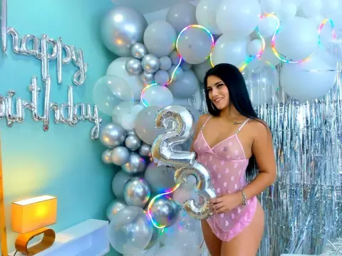 DesireLoww — Smiling woman in a pink lace bodysuit holding a silver number 23 balloon at a festive birthday party.