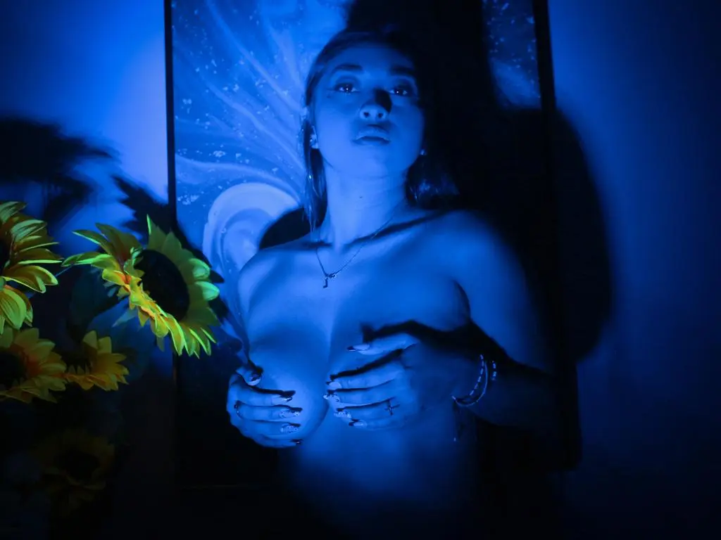 Young woman in moody blue lighting posing in front of a cosmic painting in a dark room.
