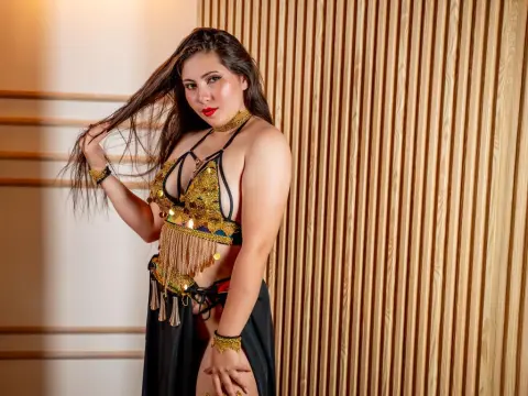 MaryxLight — MaryxLight poses in a gold and black belly dance outfit, running her hand through her long dark hair against a slatted wooden wall.