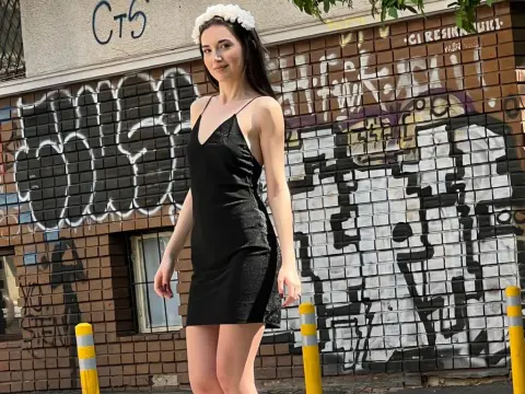Young woman in a black slip dress standing against a graffiti brick wall in bright daylight.