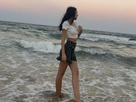 Young woman in white crop top and polka dot shorts walking on a beach at sunset.