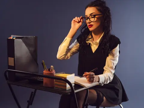 Studious young woman in glasses and white blouse writing in a notebook at a desk in a moody office setting.