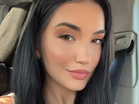 Close-up portrait of a brunette woman with natural makeup sitting in a car with a soft, serene mood.