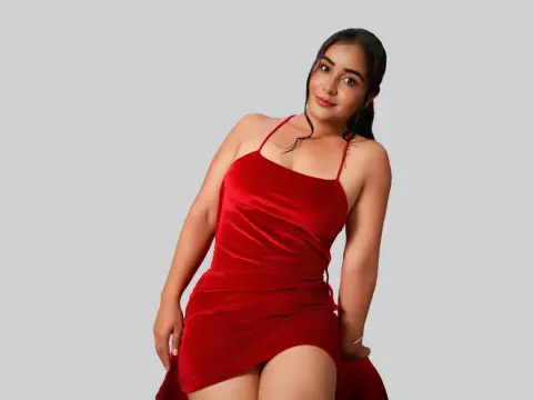 Sweet_Desire — Smiling young woman in a glamorous red velvet mini dress posing against a neutral studio background.