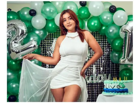 Sweet_Desire — Young woman in a white halter dress celebrating a birthday with green balloons and a cake.
