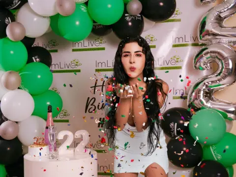 Flower_Cute — Young woman in a white dress blowing confetti at a birthday party with green and black balloons.
