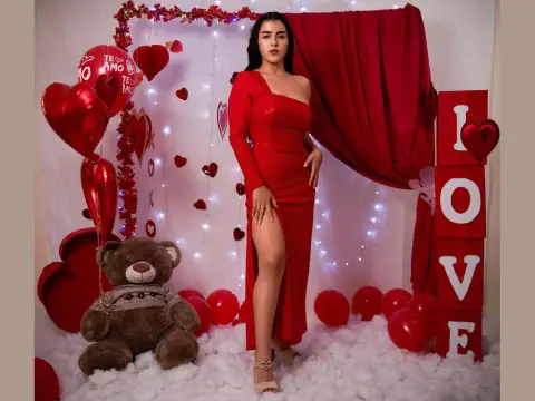 Flower_Cute — Woman in elegant red evening gown posing in romantic Valentine's Day setting with red hearts and teddy bear.