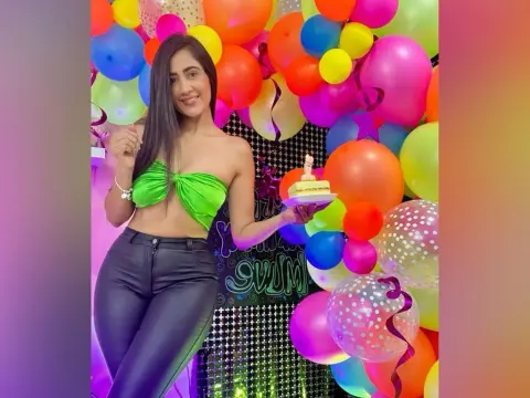 AntonelaDreamss — Smiling woman in a green bandeau top and black leather pants holding a cake amidst colorful birthday balloons.