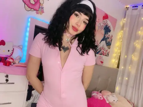 Berrylicious_ — Berrylicious_ poses in a pink short-sleeve bodysuit and white headband, showing her long dark hair and cleavage in a bedroom setting.