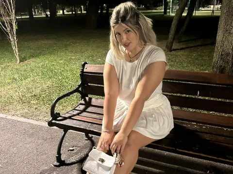Blonde woman in a white summer outfit sitting on a park bench at night under soft lighting.