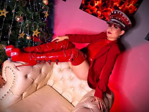 MoiraDevil32 — Glamorous woman in red suit and tall boots reclining on a cream sofa near a glowing Christmas tree.
