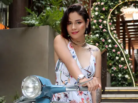 LaurenWard — Young woman in a floral sundress posing with a blue vintage scooter in a lush garden setting.